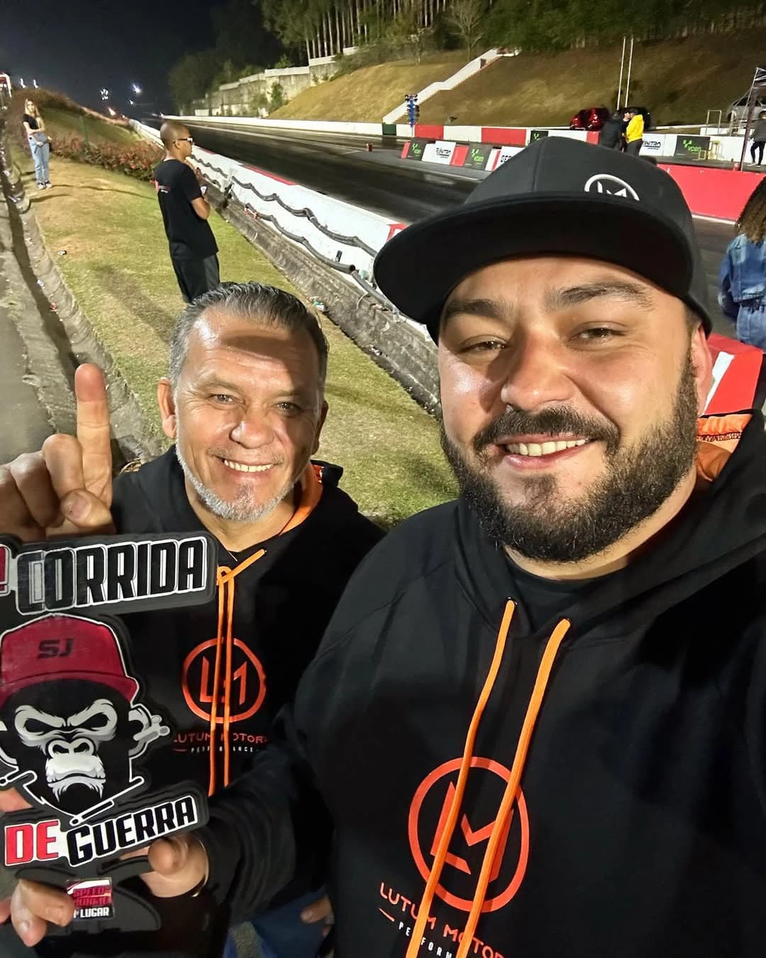 James e Thiago Lutum juntos na pista de arrancada, segurando o troféu Corrida de Guerra